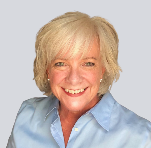 Smiling woman with short blonde hair, wearing a light blue shirt. The image conveys a friendly and approachable demeanor, suitable for professional profiles.